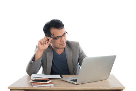 businessman holding a pen thinking sitting at his desk behind his new notebook isolated on white background.の写真素材