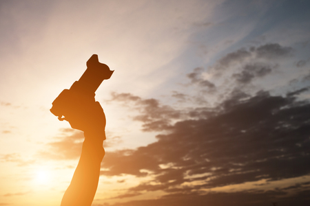 Silhouette of man hand holding camera while sunset.の写真素材