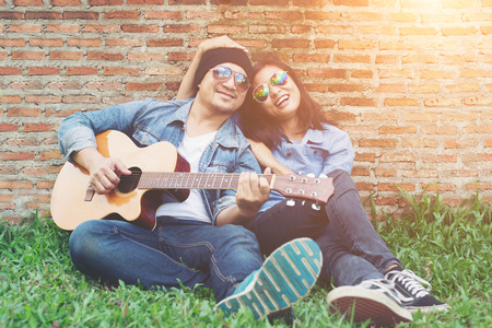 Hipster man playing guitar for his girlfriend outdoor against brick wall, enjoying together.の写真素材