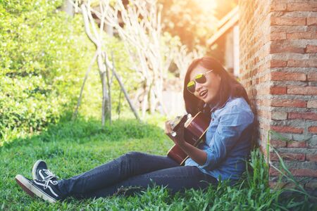 Young hipster girl sitting playing a guitar and singing.の写真素材
