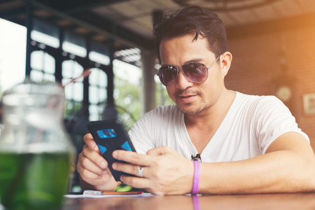 Happy young man looking at his mobile phone and smiling while sitting at cafe.の写真素材