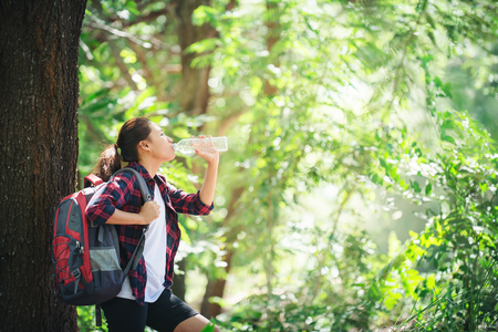 Thirsty woman having a break drinking a bottle of water during hiking in the forest.の写真素材