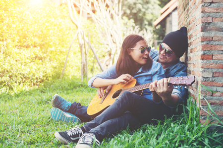 Hipster man teach playing the guitar to his girlfriend while sitting in the grass look so happy. Couple in love concept.の写真素材
