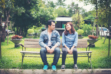 Young smiling couple looking on each other while sitting on bench, Dating time together.の写真素材