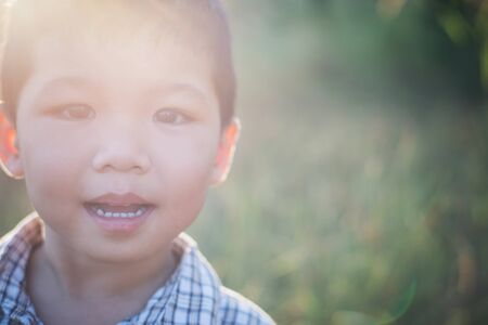 Close up of cute asian boy playing and smiling outdoors. Cute little boy on field. Summer holiday play in the park.の写真素材
