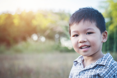 Close up of cute asian boy playing and smiling outdoors. Cute little boy on field. Summer holiday play in the park.の写真素材