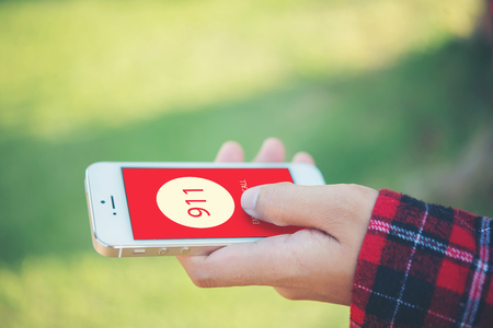 Woman holding a smartphone dialing emergency number on screen. Graphics make up on screen.の写真素材