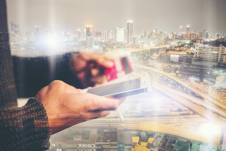 Young businessman using mobile phone shopping online with credit card, double exposure over city traffic at night.の写真素材