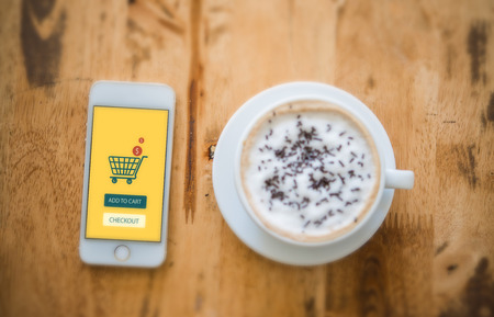Top view - Smart phone online shopping. Desk with coffee in background.の写真素材