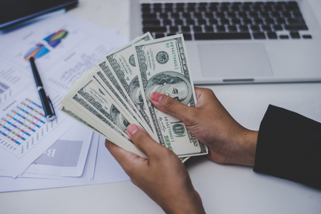 Business woman with dollars, close up sitting on her workplace with business graph on table.の写真素材