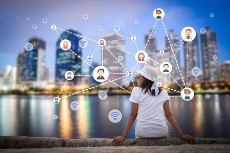 Woman sitting in the city park near the river with people and multimedia icon. Technology networking concept.の写真素材