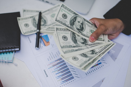 Business woman with dollars, close up sitting on her workplace with business graph on table.の写真素材