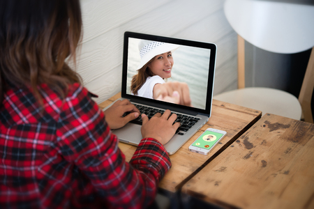 Young woman sat looking her photos from laptop while relaxing at home.の写真素材