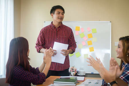 Handsome young man standing near whiteboard and pointing on the chart presentation perfect planning business with people group clapping.の写真素材