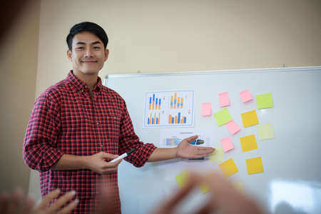 Handsome young man standing near whiteboard and pointing on the chart presentation perfect planning business with people group clapping.の写真素材