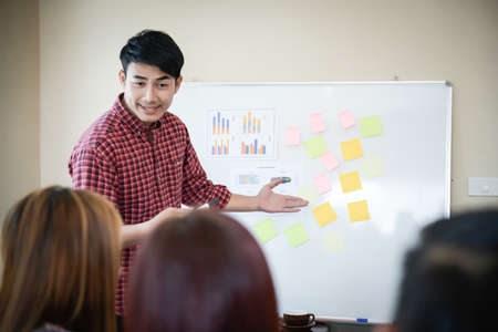 Handsome young man standing near whiteboard and pointing on the chart presentation perfect planning business with people group clapping.の写真素材