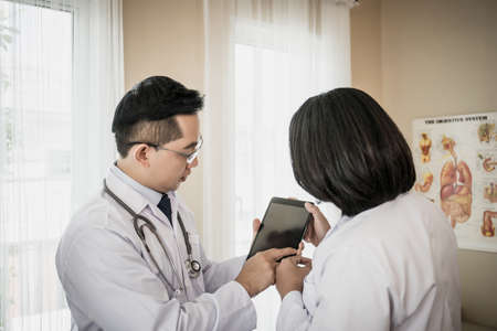 Two doctors discuss work. While watching through the tablet together in the hospital.の写真素材