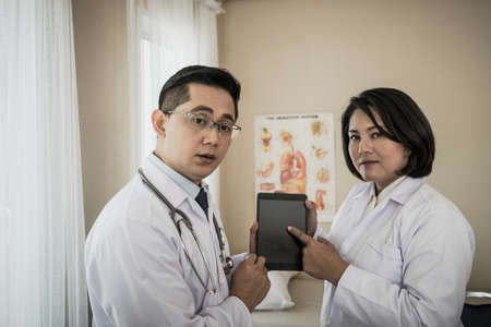 Two doctors discuss work. While watching through the tablet together in the hospital.の写真素材