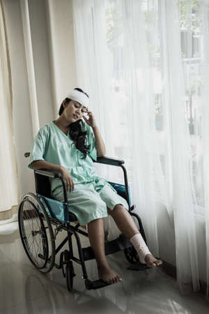Female patients having pain in her head after hospitalization sitting on wheelchair in patient's room hospital.の写真素材