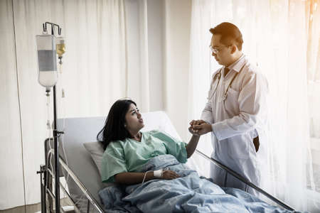Medical doctor talking to patient and  Holding her hand to comforting her. Female patient having injury lying on bed at hospital.の写真素材