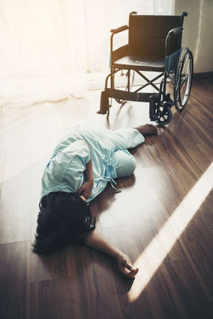 Female patients fall unconscious from a wheelchair on the floor. Heart attack, patients do not help themselves.の写真素材