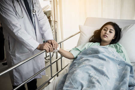 Medical doctor talking to patient and  Holding her hand to comforting her. Female patient having injury lying on bed at hospital.の写真素材