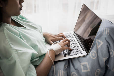 Sick woman works with laptop in hospital.の写真素材