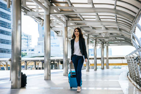 Beautiful young businesswoman walking outside public transportation station. Businesswoman traveler with suitcase on the way to the airport.の写真素材