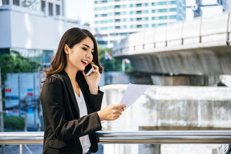 Image of busy female calling on the phone and reading document while going to workの写真素材