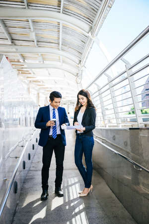 Business colleagues take a look at the work in the tablet while walking to the office together.の写真素材