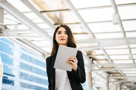 Attractive business woman using a digital tablet while standing in front of office building.の写真素材