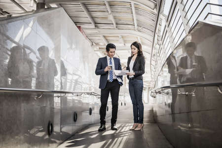 Business colleagues take a look at the work in the tablet while walking to the office together.の写真素材