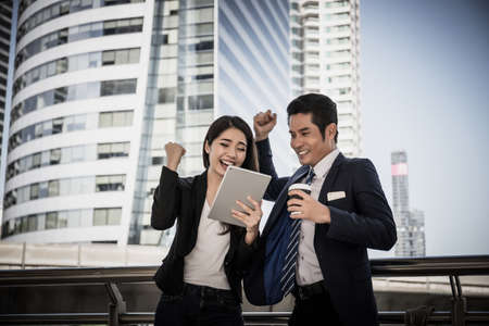 Young asian business colleges look at work in tablet together happy achievement and success.の写真素材