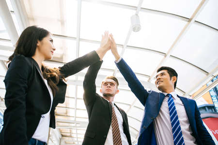 Successful business team is giving high five and smiling while standing in front of office.