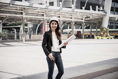 beautiful woman engineer holding paper plan is standing  in front of an industrial building backgroundの写真素材