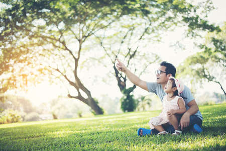 happy father and daughter pointing with finger and looking at something in parkの写真素材