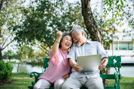 Cheerful senior woman and man using digital tablet on bench at the parkの写真素材