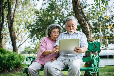 Cheerful senior woman and man using digital tablet on bench at the parkの写真素材