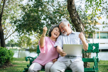 Cheerful senior woman and man using digital tablet on bench at the parkの写真素材
