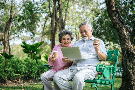 Cheerful senior woman and man using digital tablet on bench at the parkの写真素材