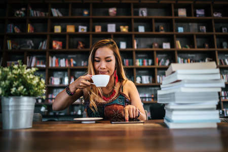 woman is holding a cup of hot cappuccino and reading a book, Business woman read a book in coffee shopの写真素材