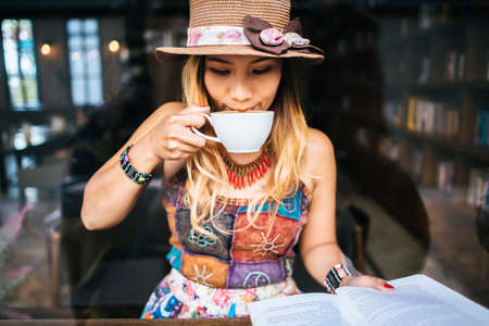 woman is holding a cup of hot cappuccino and reading a book, Business woman read a book in coffee shopの写真素材