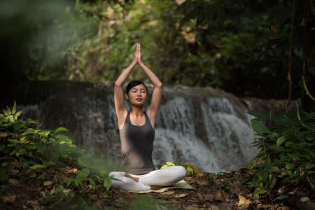 Young woman in yoga pose sitting near waterfallの写真素材