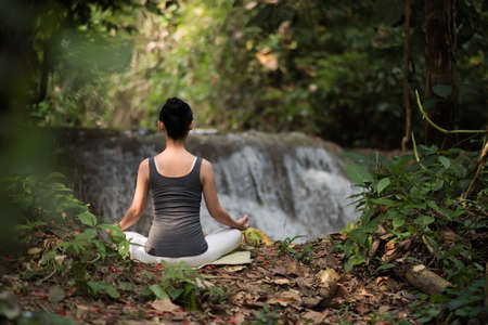 Young woman in yoga pose sitting near waterfallの写真素材