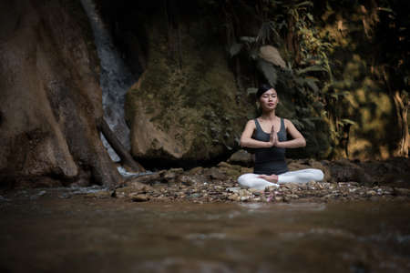 Young woman in yoga pose sitting near waterfallの写真素材