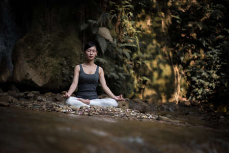 Young woman in yoga pose sitting near waterfallの写真素材