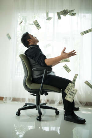Happy business man very rich guy throw money dollar bills in air like rain money bill and banknotes US dollar bill on the table - business success conceptの写真素材