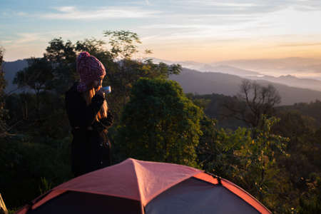 Young woman is enjoying cup of coffee outside with beautiful view of mountainsの写真素材
