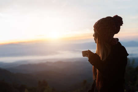 Young woman is enjoying cup of coffee outside with beautiful view of mountainsの写真素材