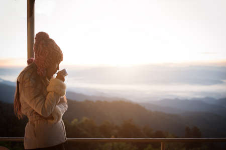Young woman is enjoying cup of coffee outside with beautiful view of mountainsの写真素材